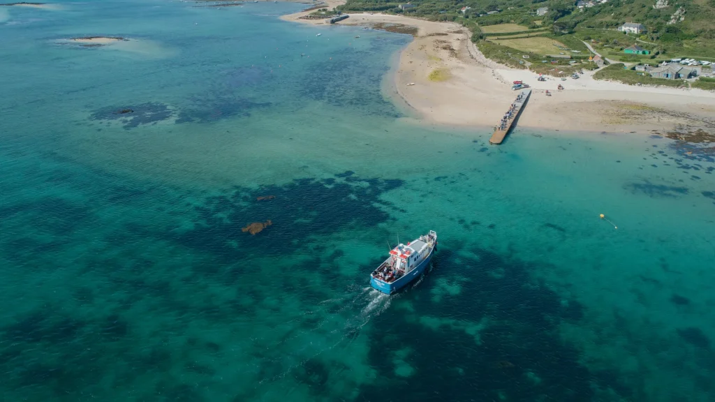 A passenger boat crossing turquoise water towards the quay on Bryher, seen from the air