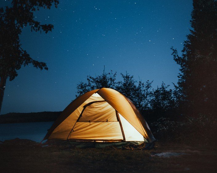 A lit tent under a starry night sky beside the water