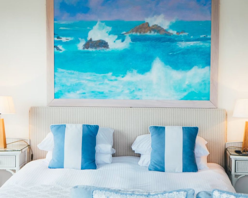 Bedroom with blue striped cushions beneath a seascape painting